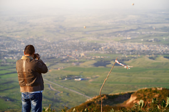 Traveller photographing mountain village and hot air balloons