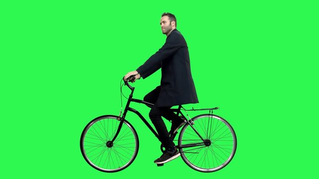 A Cute man riding a bicycle over a green screen, looking around and upwards, waving hello. No motion blur for optimal keying.