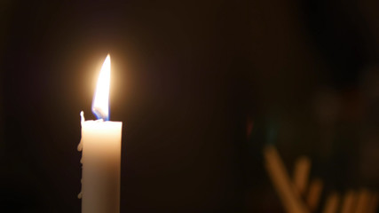 Close-up of candle flame in black background, someone moving behind the candle