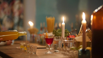 Professional bartender pouring orange drink into a small glasses in the bar with soft interior lighting