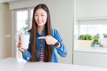 Beautiful Asian woman drinking a fresh glass of milk very happy pointing with hand and finger