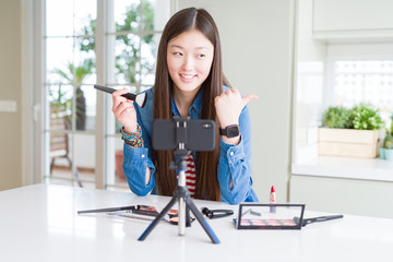 Beautiful Asian influencer woman recording make up tutorial using smartphone camera pointing and...