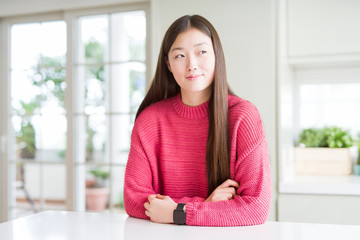 Beautiful Asian woman wearing pink sweater on white table smiling looking side and staring away thinking.