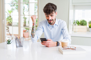 Young business man using smartphone sending a message screaming proud and celebrating victory and...