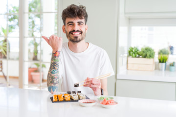 Young man eating asian sushi from home delivery pointing and showing with thumb up to the side with happy face smiling
