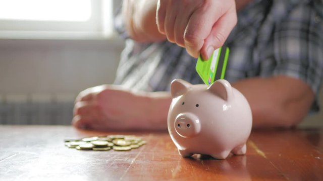 Woman putting credit card into piggy bank. The concept of saving money and investment.