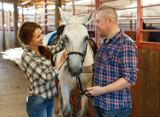 Couple of farmers  standing  with white horse  at stabling indoor