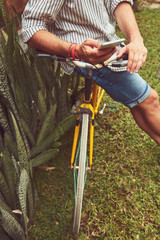 Modern man using cellphone while sitting on the grass with old bicycle.