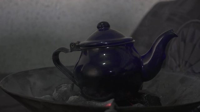 Saharaui man making tea with teapot and charcoal fire.