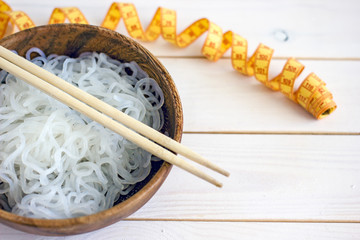 Chinese dietary noodles shirataki konjak in a wooden bowl with chinese chopsticks. Near the tape to measure the body. Gluten-free diet for weight loss.
