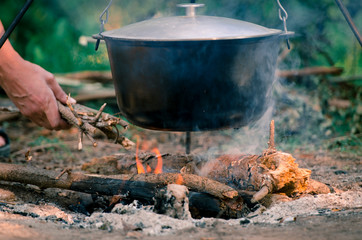 A man's hand kindles a fire under a pan, which stands on a fire.