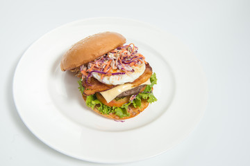 A delicious beef burger  with lettuce ,bacon ,cheese and topped with a fried egg on white