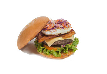 A delicious beef burger  with lettuce ,bacon ,cheese and topped with a fried egg on white