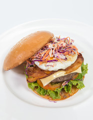 A delicious beef burger  with lettuce ,bacon ,cheese and topped with a fried egg on white
