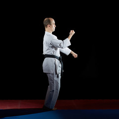 Fototapeta na wymiar Adult athlete trains formal karate exercises on red and blue tatami