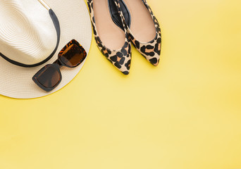 Straw hat, sunglasses and leopard print shoes on yellow background, copy space for text