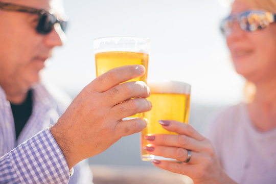 Retired Couple Drinking Beer In Sunny Day - Focus On Clinking Glasses