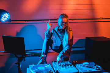 cheerful stylish dj woman in glasses gesturing while touching dj mixer