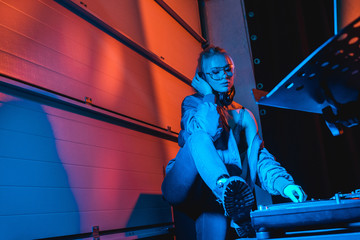 pensive dj woman in glasses touching dj mixer while listening music in headphones