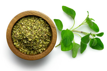 Dried chopped oregano in dark wood bowl next to fresh oregano leaves isolated on white from above.