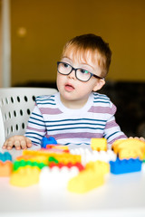 Little baby boy with down syndrome with big blue glasses playing with colorful bricks