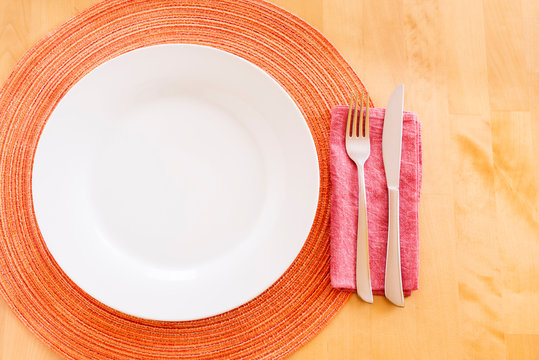 Ein weißer leerer Teller mit Besteck und Serviette auf einem Holztisch