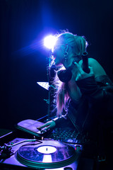 cheerful and stylish dj woman holding bottle while touching dj equipment in nightclub