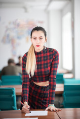 Young woman with red lipstick working standing in the office by the table and holding a pen