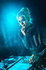 beautiful blonde dj girl using dj equipment in nightclub with smoke