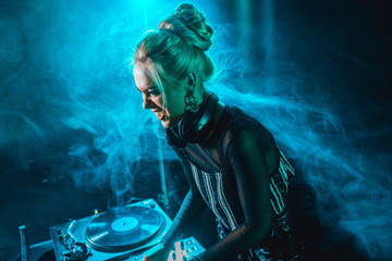 Obraz premium angry blonde dj girl using dj equipment in nightclub with smoke