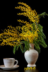 On the table is a vase with mimosa on a black background.