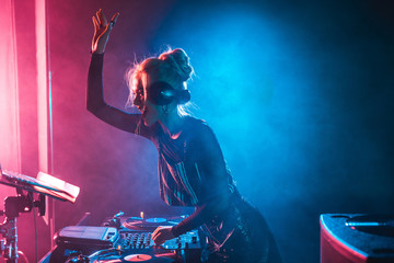 happy dj girl with blonde hair using dj mixer in nightclub with smoke - obrazy, fototapety, plakaty