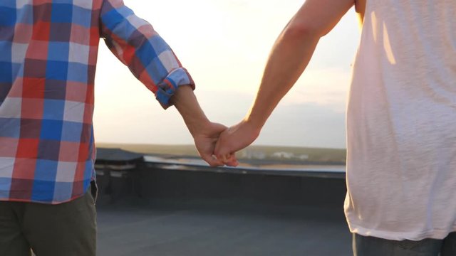 Friends holding hands of each other during running and rejoices life with beautiful sunset at background. Unrecognizable gay couple showing joy and happiness outdoor. Young men spending time together