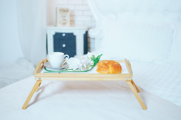 Breakfast tray in bed: white cup, croissants and flowers