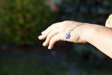 Female hand is holding a blue necklace. Enamel decoration
