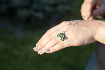 Female hand is holding a blue necklace. Enamel decoration