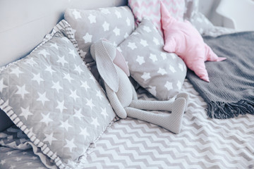 Toy gray rabbit and pillows on a gray children's bed