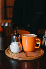 Coffee Raf in an orange mug, with sugar bowl and spoon, on wooden stand in coffee shop