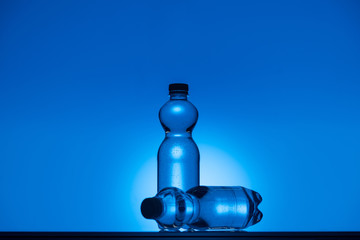 toned image of plastic water bottles on neon blue background with copy space and backlit