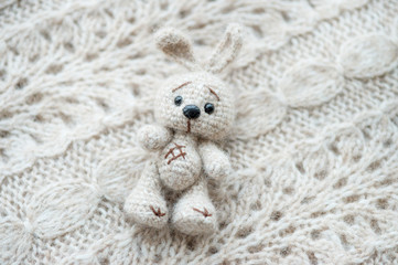 Knitted white hare is lying on a light knitted handmade fabric. There is a free space.