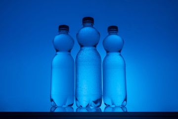 toned image of plastic bottles with water on neon blue background