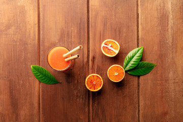 A glass of fresh orange juice with blood oranges, green leaves, and two bamboo straws, shot from the top on a dark wooden background with copy space