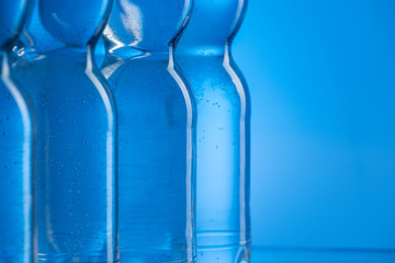 close up of plastic water bottles with bubbles in row on blue background with copy space