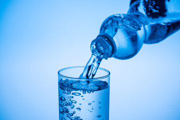 water pouring from plastic bottle in glass on blue background with copy space