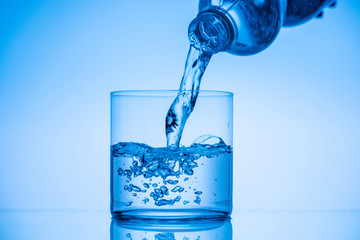 water pouring from plastic bottle in drinking glass on blue background