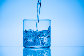 toned image of water pouring in glass on blue background with copy space