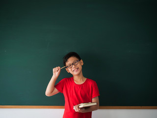 Asian boy with book on blackboard background education school classroom concept