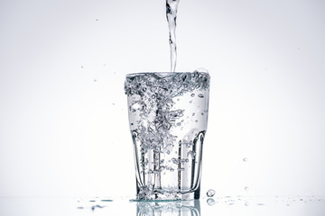 water pouring in full glass on white background with backlit and splashes
