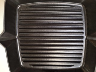 Fototapeta premium New empty grill pan with structured surface and selective focus. Square iron textured grill. Grilled steel backdrop 