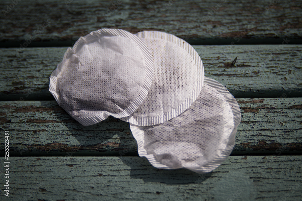 Wall mural Three round teabags containing black tea leaves on w painted wooden background.  Convenience, hot drink, relaxing concepts.